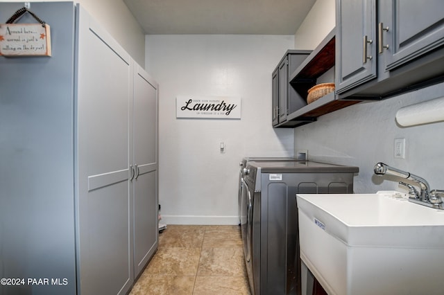 laundry room with washer and clothes dryer, light tile patterned flooring, cabinets, and sink