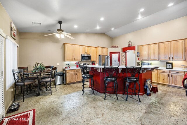 kitchen with a kitchen breakfast bar, stainless steel appliances, vaulted ceiling, ceiling fan, and a kitchen island