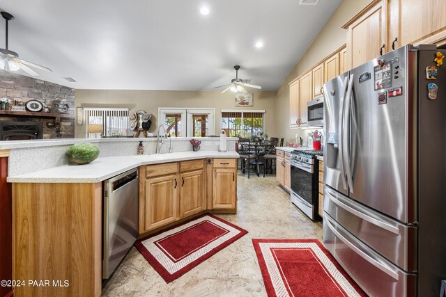 kitchen featuring ceiling fan, a fireplace, stainless steel appliances, and vaulted ceiling