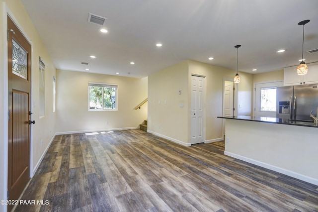 unfurnished living room featuring plenty of natural light, dark wood finished floors, and visible vents