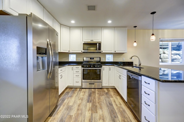 kitchen with visible vents, white cabinets, a peninsula, stainless steel appliances, and a sink