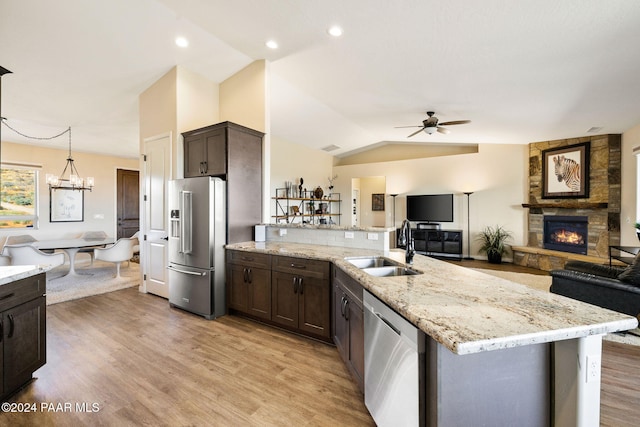 kitchen with sink, a stone fireplace, lofted ceiling, appliances with stainless steel finishes, and light wood-type flooring