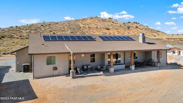 rear view of house featuring outdoor lounge area, solar panels, a mountain view, central air condition unit, and a patio area