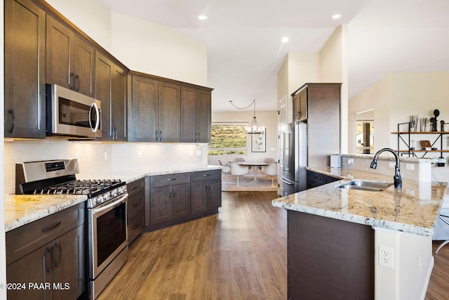 kitchen featuring light stone countertops, appliances with stainless steel finishes, light wood-type flooring, sink, and decorative light fixtures