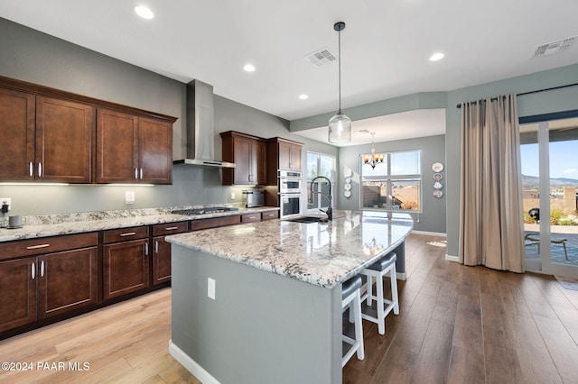 kitchen featuring a kitchen island with sink, plenty of natural light, wall chimney exhaust hood, and stainless steel appliances