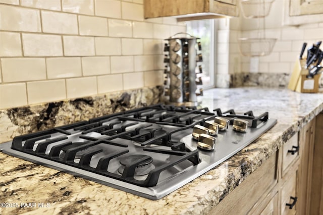 details with light stone counters, light brown cabinetry, backsplash, and stainless steel gas cooktop