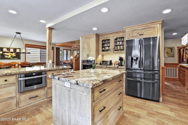 kitchen with refrigerator with ice dispenser, ceiling fan, light stone counters, a kitchen island, and stainless steel oven