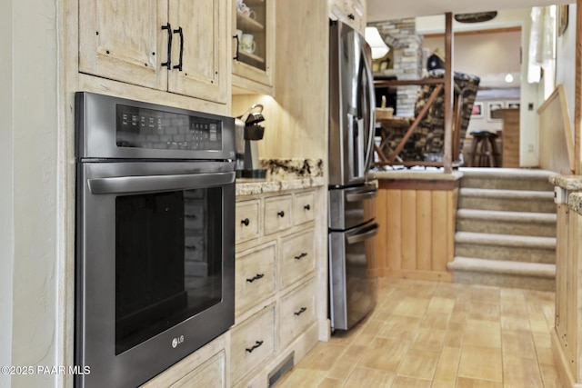 kitchen featuring stainless steel appliances, light brown cabinetry, light stone countertops, and light wood-type flooring