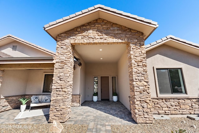 entrance to property featuring stucco siding, stone siding, and a patio