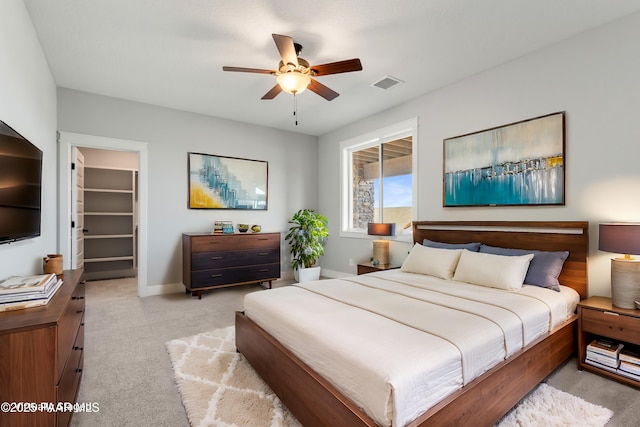 bedroom with visible vents, a walk in closet, ceiling fan, baseboards, and light carpet