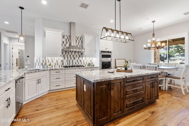 kitchen with visible vents, light wood-style floors, white cabinets, wall chimney range hood, and decorative backsplash