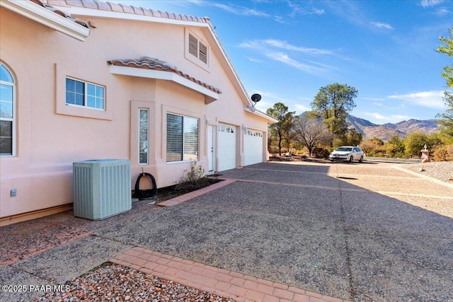 view of side of property with central AC unit, a mountain view, a tile roof, driveway, and stucco siding