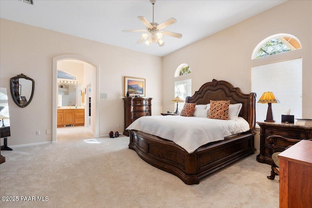 bedroom featuring ceiling fan, ensuite bathroom, arched walkways, light carpet, and baseboards