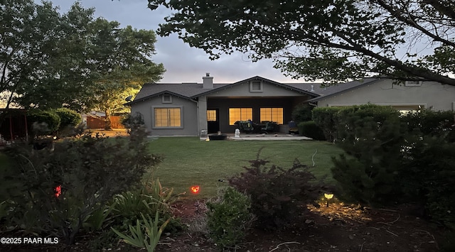 back house at dusk featuring a patio area and a yard