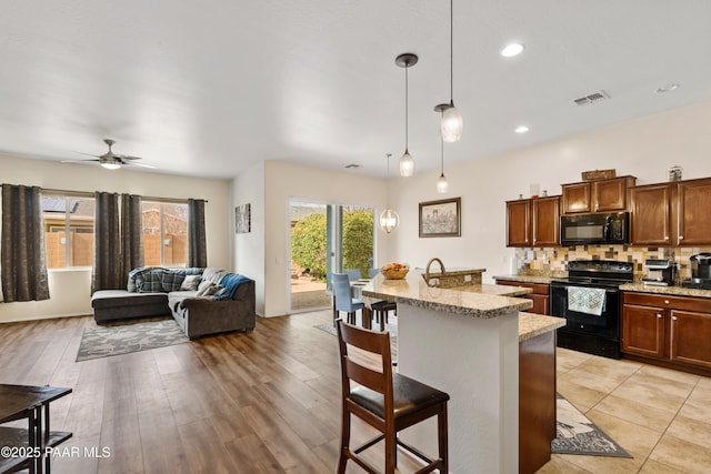 kitchen featuring light stone countertops, decorative backsplash, a kitchen bar, black appliances, and visible vents