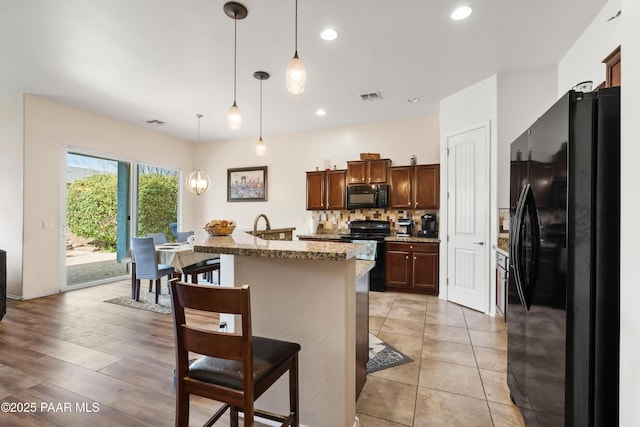 kitchen with decorative backsplash, a center island with sink, black appliances, a breakfast bar, and light stone counters