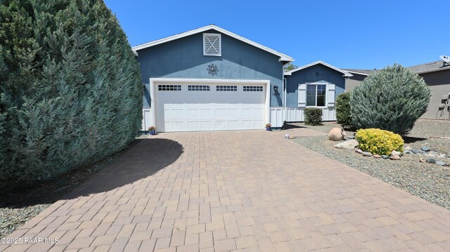 single story home featuring a garage, stucco siding, and decorative driveway