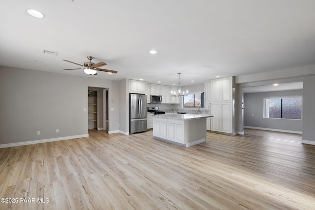 kitchen with ceiling fan with notable chandelier, stainless steel appliances, pendant lighting, a center island, and white cabinetry