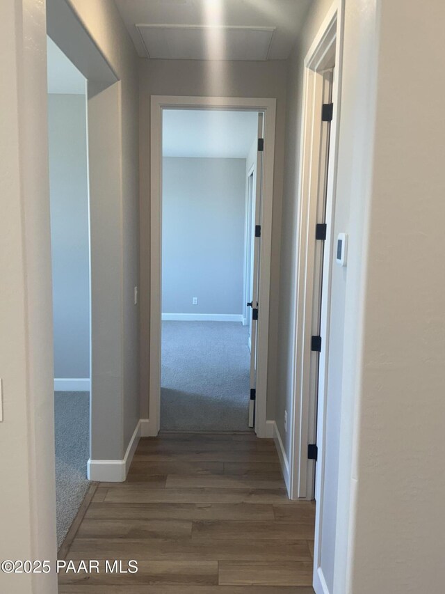 hall with attic access, wood finished floors, baseboards, and carpet
