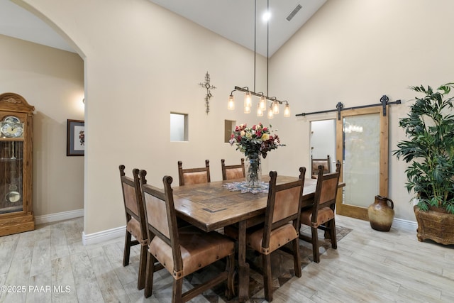 dining space featuring high vaulted ceiling, light hardwood / wood-style floors, and a barn door