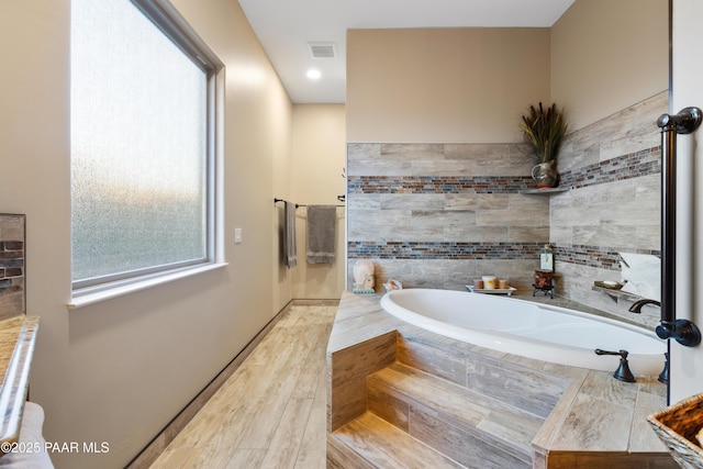 bathroom featuring a relaxing tiled tub and hardwood / wood-style floors