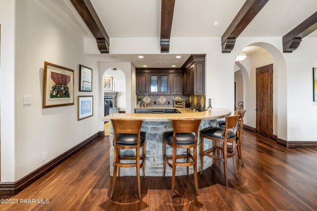 kitchen with beam ceiling, dark brown cabinetry, dark wood-type flooring, backsplash, and kitchen peninsula