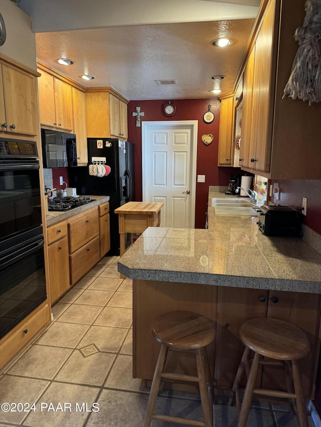 kitchen with black appliances, sink, light tile patterned floors, a kitchen bar, and kitchen peninsula