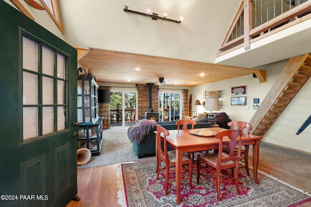 dining space with a wood stove, ceiling fan, wood-type flooring, and lofted ceiling