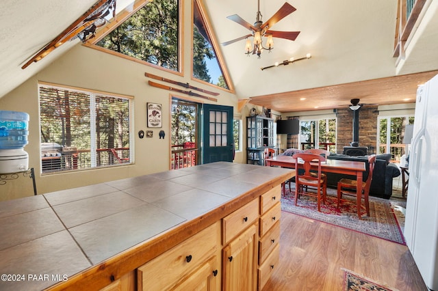 kitchen featuring a wood stove, light hardwood / wood-style flooring, high vaulted ceiling, white refrigerator, and tile countertops