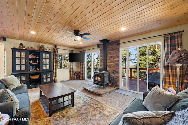 carpeted living room with a wood stove, ceiling fan, and wood ceiling