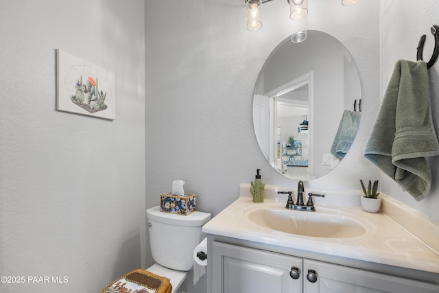 bathroom featuring toilet, a textured wall, and vanity