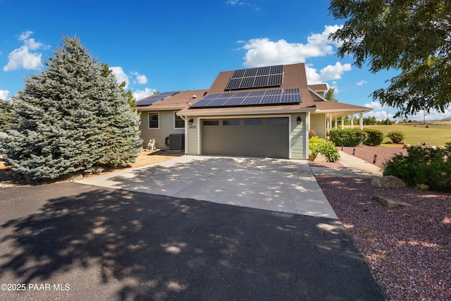 view of front of home featuring a garage, roof mounted solar panels, cooling unit, and concrete driveway