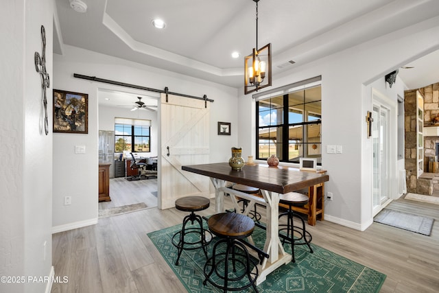 dining area with a tray ceiling, visible vents, light wood-style flooring, a barn door, and baseboards