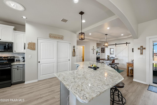 kitchen with black appliances, a barn door, white cabinetry, and a center island