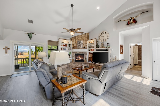 living area featuring visible vents, ceiling fan, a stone fireplace, light wood-style floors, and high vaulted ceiling