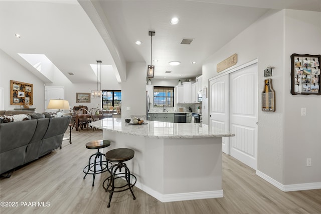 kitchen featuring hanging light fixtures, light wood-style floors, white cabinetry, and light stone counters