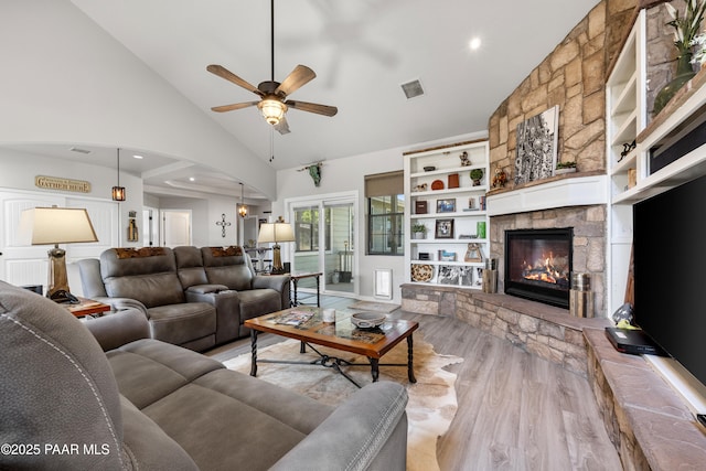 living room featuring ceiling fan, high vaulted ceiling, light wood-style flooring, a fireplace, and visible vents