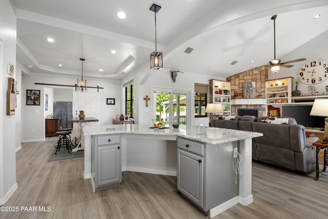 kitchen with a barn door, gray cabinetry, a kitchen island, open floor plan, and light stone countertops