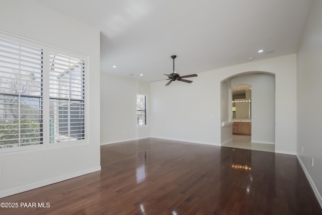 unfurnished room featuring arched walkways, ceiling fan, wood finished floors, and a healthy amount of sunlight