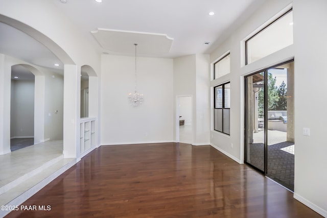 unfurnished room with a towering ceiling, wood finished floors, baseboards, a notable chandelier, and recessed lighting