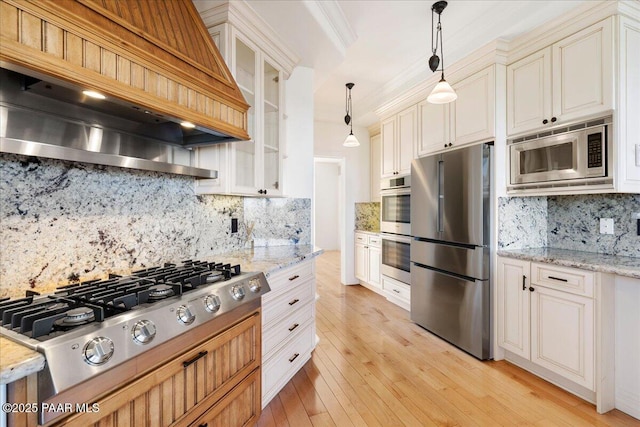 kitchen with pendant lighting, appliances with stainless steel finishes, light wood finished floors, light stone countertops, and custom exhaust hood