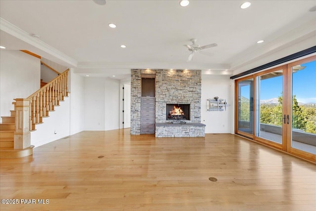 unfurnished living room with wood finished floors, recessed lighting, a stone fireplace, stairs, and crown molding