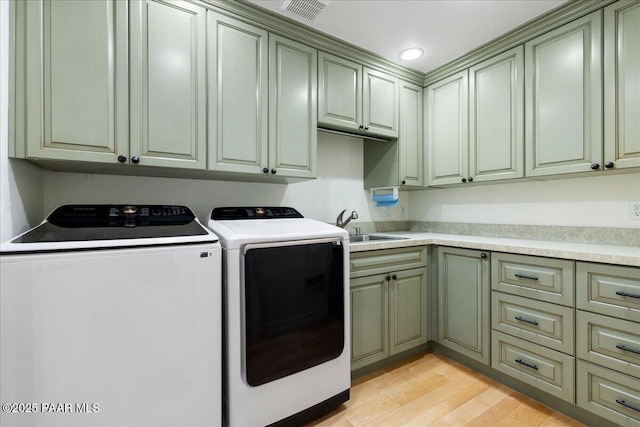 clothes washing area with light wood-type flooring, visible vents, washer and clothes dryer, a sink, and cabinet space