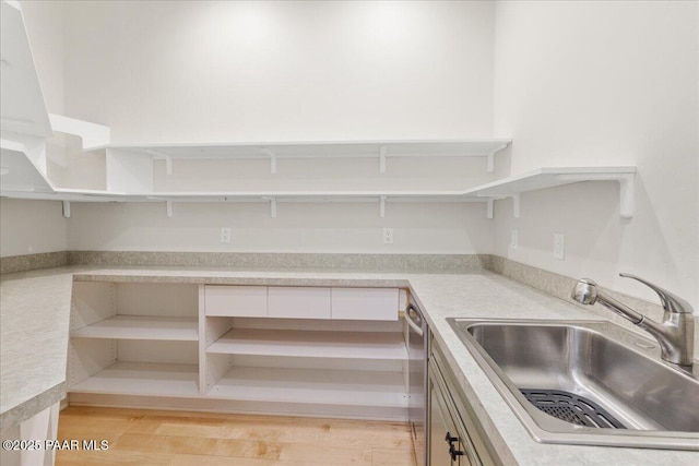 kitchen featuring open shelves, light countertops, stainless steel dishwasher, white cabinetry, and a sink