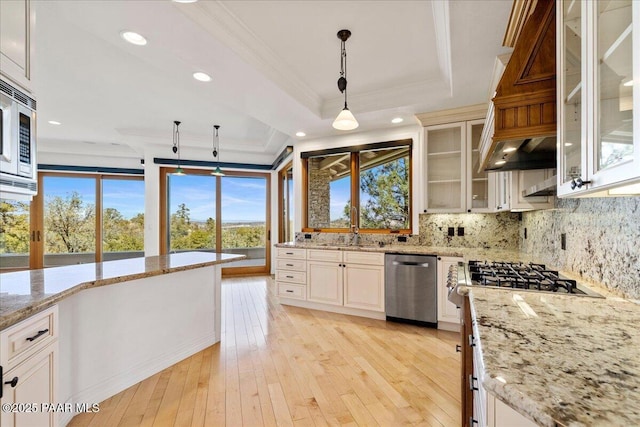 kitchen featuring light wood-type flooring, ornamental molding, a sink, stainless steel appliances, and a raised ceiling