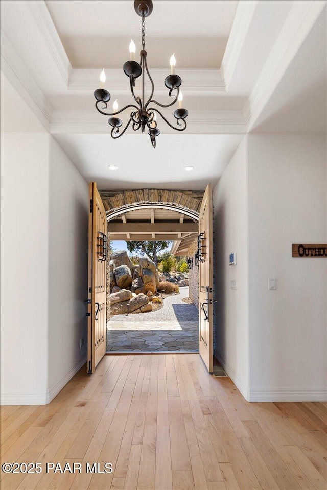 foyer with a tray ceiling, a notable chandelier, crown molding, and light wood-style floors