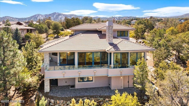 back of house with a tiled roof, a chimney, a sunroom, a patio area, and a mountain view