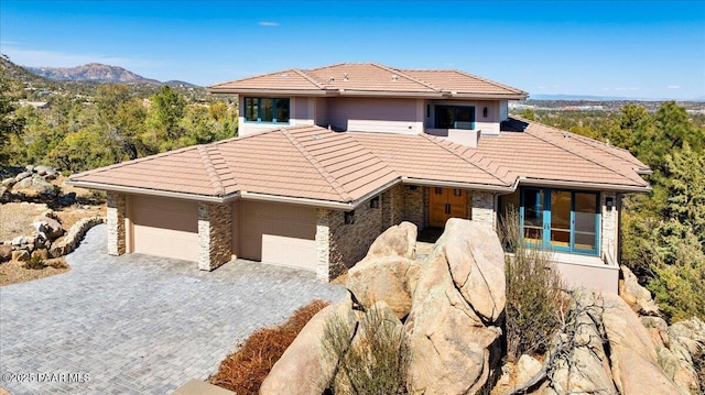 prairie-style home with decorative driveway, stone siding, an attached garage, and a tile roof