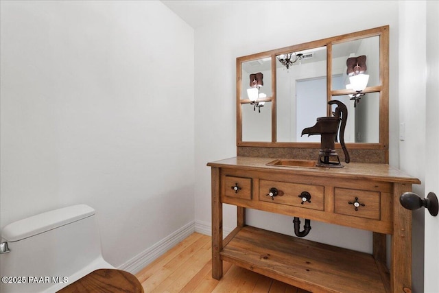 bathroom with toilet, vanity, baseboards, and wood-type flooring