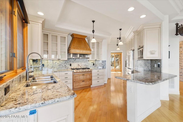 kitchen with a peninsula, light wood-style flooring, a sink, custom range hood, and appliances with stainless steel finishes